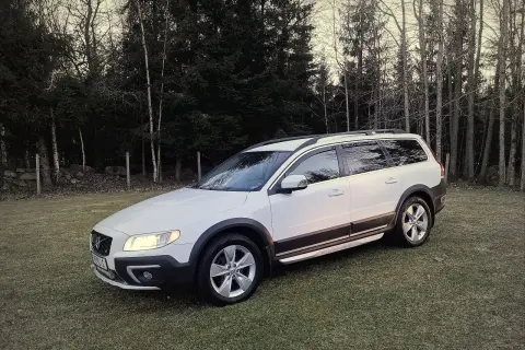 Vit Volvo XC70 parkerad på en gräsmatta med skog i bakgrunden. Kanske ett volvo d4 motor problem gör att den står stilla.