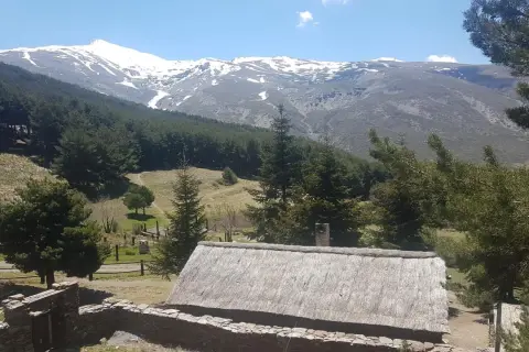 Casa rural con tejado de paja y montañas nevadas al fondo, un paisaje idílico de la fuente alta Sierra Nevada.