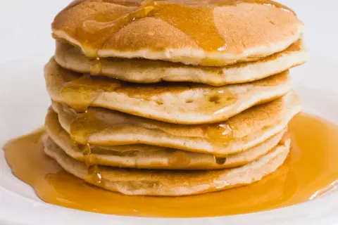 Pila di pancake proteici dorati, inzuppati di sciroppo d'acero che cola.