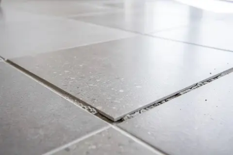 Carrelage gris, certaines dalles se soulèvent, révélant le gravier en dessous. Un signe de vieillissement, peut-être une décennale carrelage à prévoir.