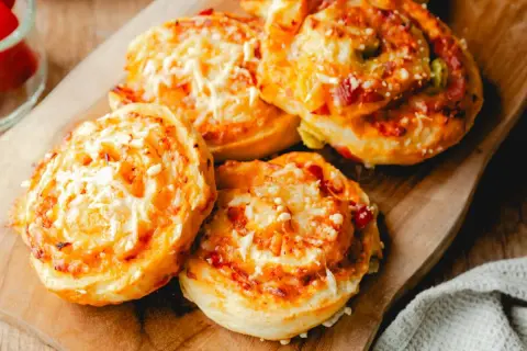 Leckere Pizzaschnecken aus Pizzateig, überbacken mit Käse und Tomaten, liegen auf einem Holzbrett.