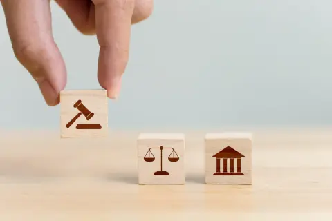Dłoń układa kostki symbolizujące prawo, sprawiedliwość i sąd. Decyzja o jurysdykcji.