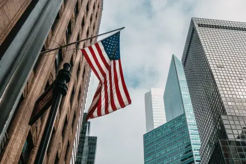 Amerykańska flaga powiewa między drapaczami chmur. Zastanawiasz się, ile kosztuje ubezpieczenie w USA?