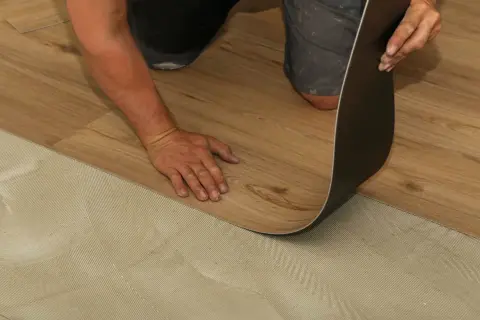 Hand verlegt Laminat auf PVC-Boden. Der Kleber ist auf dem Untergrund aufgetragen, bereit für das neue Bodenmuster.