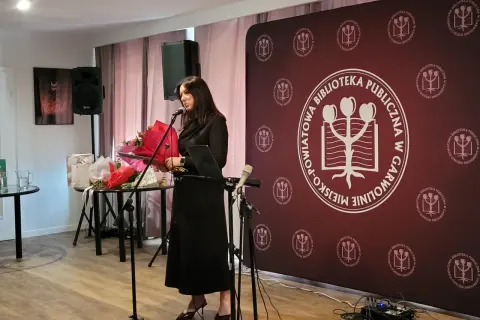 Kobieta przemawia na tle baneru z logo biblioteki, podczas wydarzenia w Garwolinie. Wgm rejestracja.