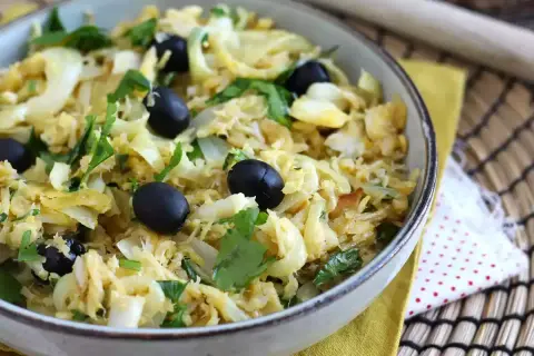 Un plat de bacalhau à bras, mélange savoureux de morue effilochée, d'oignons, d'œufs brouillés et d'olives noires, garni de persil frais.
