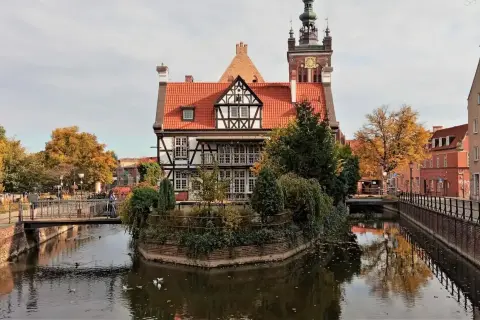 Gdańsk ciekawostki: malowniczy dom z muru pruskiego nad kanałem, w tle wieża kościelna i jesienne drzewa.