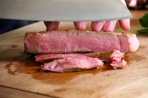 Ein saftiges Kalbskotelett sous vide wird auf einem Holzbrett in Scheiben geschnitten.