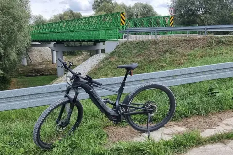 Rower elektryczny czeka na przygodę na trasie w Kazimierzu Dolnym. Zielony most w tle zaprasza do odkrywania malowniczych zakątków.