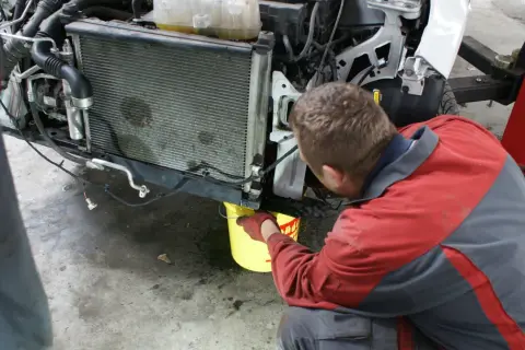 Mechanik w rękawiczkach nalewa płyn do chłodnicy, pokazując, jak działa uszczelniacz do chłodnic.
