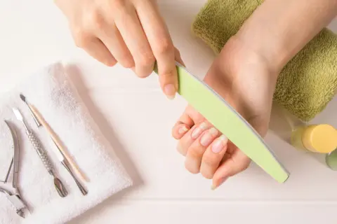 Dłonie z naturalnymi paznokciami, pilniczek, cążki i inne akcesoria do manicure. Dowiedz się, jak szybko zapuścić paznokcie.