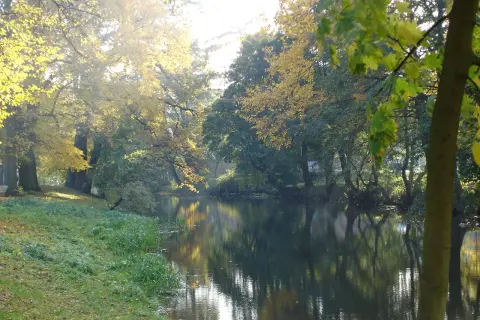 Jesienne słońce rozświetla miasto nad Iną. Drzewa w złotych barwach odbijają się w spokojnej wodzie.