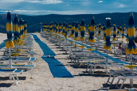 Rzędy leżaków i parasoli na plaży, jakby typowy polak na wakacjach szukał swojego miejsca.