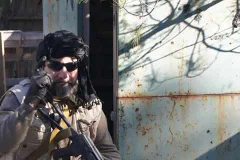 Hombre con turbante negro, gafas de sol y chaleco táctico, listo para una partida de milsim airsoft.