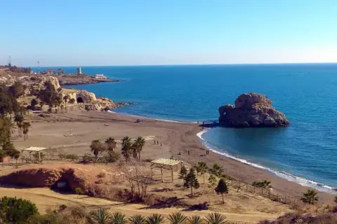 La playa Peñón del Cuervo, con su icónica roca en el mar, invita a pasear por su arena oscura bajo un cielo azul.