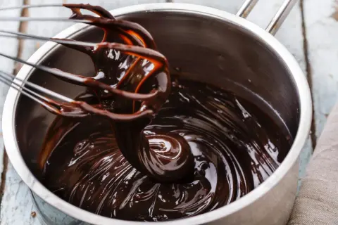 Ein Schneebesen rührt glänzende, dunkle schoko ganache in einem Topf.