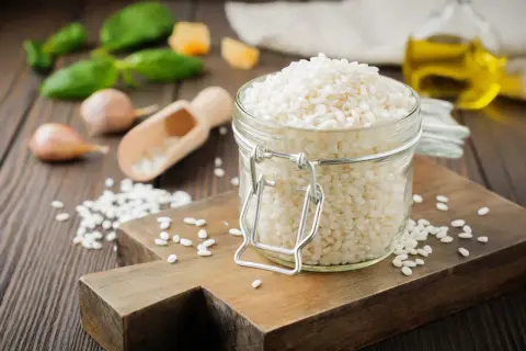 Słoik pełen ryżu **arborio**, idealnego do kremowego risotto. Obok czosnek, bazylia i oliwa.