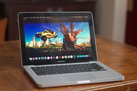 A MacBook Pro displays the "Speed Racer" trailer on the IINA player, showing a futuristic city and a car mid-explosion.
