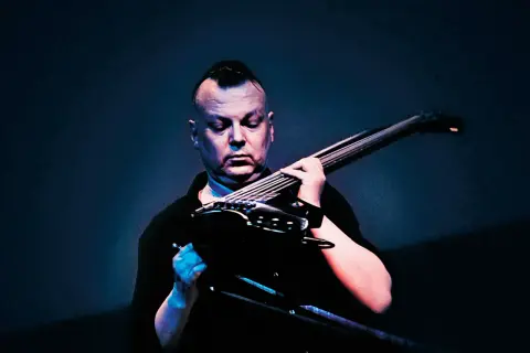 Kasper Toeplitz, z charakterystycznym irokezem, skupiony na grze na basie elektrycznym.