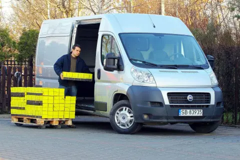 Mężczyzna rozładowuje żółte paczki z furgonetki Fiat Ducato 2.3.