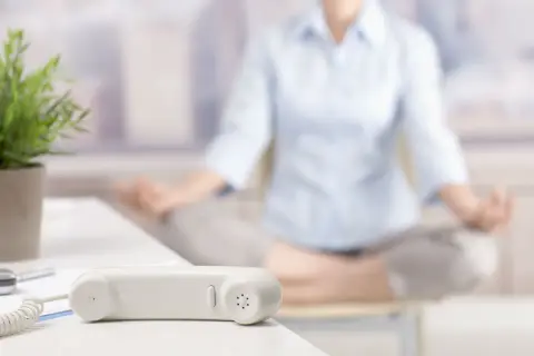 En person mediterar på kontoret. En telefonlur och en växt syns i förgrunden. En pausgympa på jobbet kan ge ny energi.