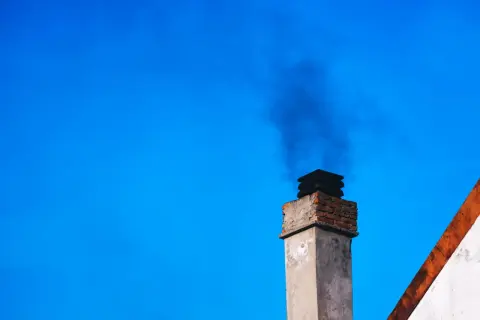 Dym z komina, być może dzięki zastosowaniu filtra kominowego zamiast wymiany pieca, unosi się na tle błękitnego nieba.