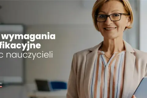 Uśmiechnięta nauczycielka w okularach trzyma tablet w sali lekcyjnej.