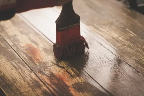 Brocha aplicando una capa de imprimación sobre tablones de madera rústica, preparándolos para un nuevo acabado.