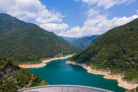 Imponente diga sul lago di Valvestino, circondato da montagne verdi e un cielo azzurro con nuvole bianche.
