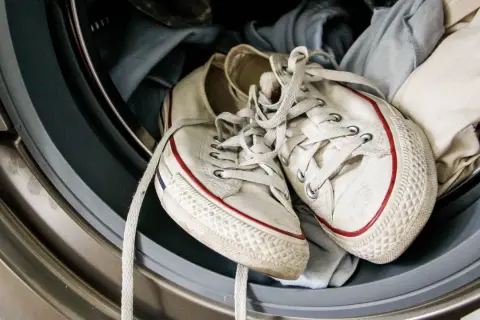 Weiße Turnschuhe mit roten Streifen liegen in der Waschmaschine, bereit zum Laufschuhe waschen.