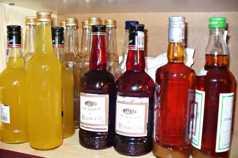 Rząd butelek z różnymi alkoholami, w tym żółtymi nalewkami i ciemnymi, jak czarna wódka.