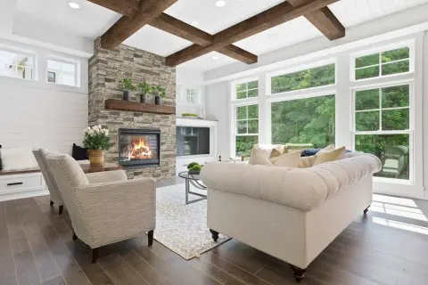 Cozy living room with a stone fireplace, tufted sofa, and an accent ceiling with exposed wooden beams.
