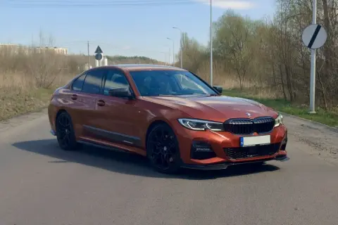 Pomarańczowe BMW 330i G20 na drodze, z widocznymi czarnymi felgami i detalami aerodynamicznymi.