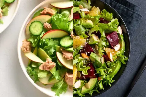 Dos ensaladas vibrantes: una con aguacate, remolacha y naranja, y otra con lechuga, manzana, pepino y atún.