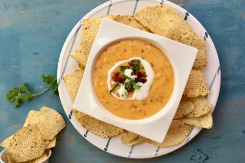 Salsa de queso cremosa en un tazón blanco, rodeada de totopos y adornada con crema y cilantro.
