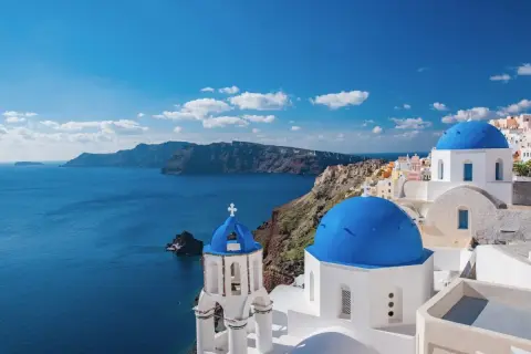 Blaue Kuppeln und weiße Gebäude auf Santorini, ein Traumziel für Griechenland Reisetipps. Die Caldera im Hintergrund.