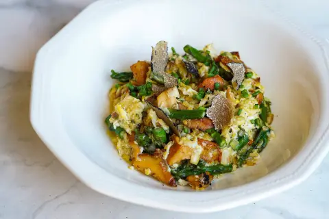 Delicioso revuelto de cantharellus con espárragos, trufa negra y cebollino, servido en un plato blanco.