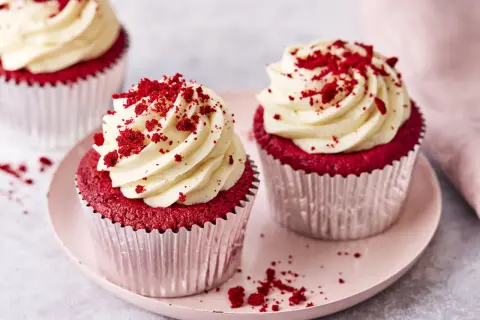 Zwei köstliche red velvet cupcakes mit cremiger Glasur und roten Krümeln, auf einem rosa Teller.