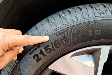Palec wskazuje na oznaczenia opon: 215/60 R16. Informacje te pomagają dobrać odpowiednie ogumienie.