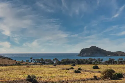 Paisaje árido del desierto Cabo de Gata con mar azul y una isla rocosa al fondo.