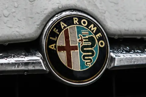 Klasyczne alfa romeo logo z krzyżem i wężem, błyszczące mimo kropel deszczu na karoserii.