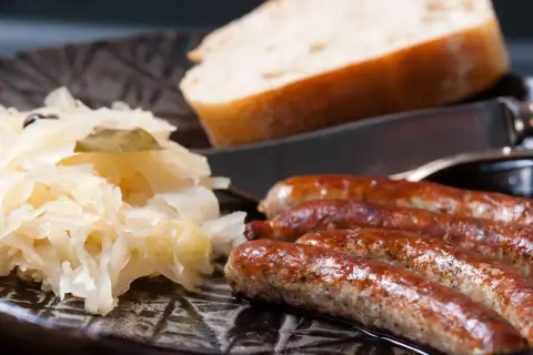 Herzhafte Bratwurst mit Sauerkraut und Brot auf dunklem Teller, bereit zum Genuss.