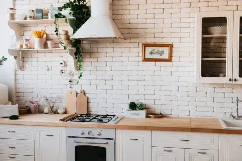 Inspiracja do tego, jak zrobić blat kuchenny z płytek ceramicznych. Jasna kuchnia z drewnianym blatem, białą cegłą i roślinami.