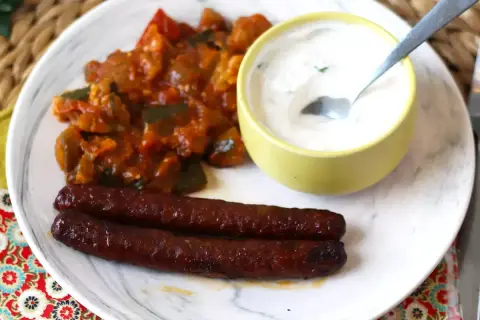 Dos salchichas merguez que es picantes, acompañadas de un guiso de verduras y una salsa cremosa.