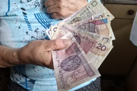 Dłoń trzyma polskie banknoty, symbolizujące środki na życie, być może jako zus renta rodzinna po mężu.