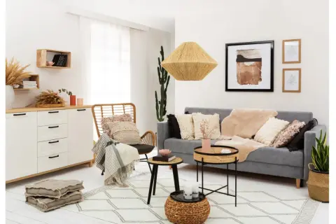 Przytulny salon w stylu rustykalnym z szarą kanapą, wiklinowym fotelem i dekoracjami z naturalnych materiałów.