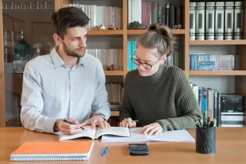 Młoda para uczy się przy biurku, otoczona książkami.