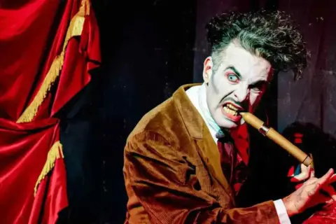 Actor con maquillaje de terror y traje marrón muerde un puro, listo para el circo del terror Zaragoza.