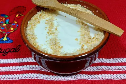 Delicioso serradura portuguesa en cuenco de barro, espolvoreado con galleta triturada y una cuchara de madera.