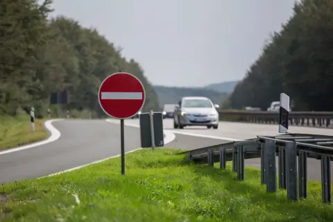 Znak b2, zakaz wjazdu, stoi przy krętej drodze. Samochody jadą w tle.
